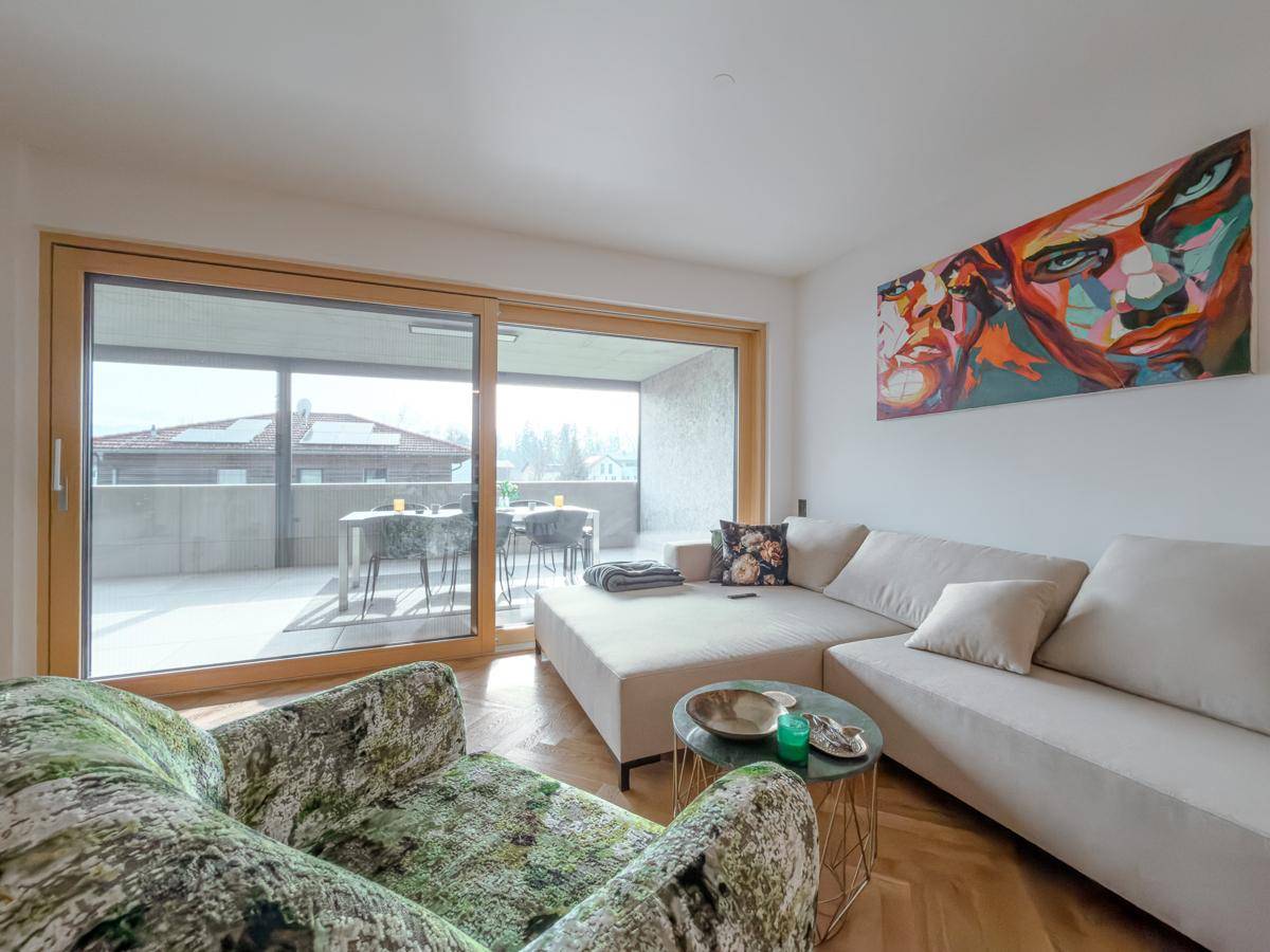 Helles Wohnzimmer mit gemütlicher Sitzecke, großem Schiebefenster und Zugang zur Terrasse mit Bergblick.