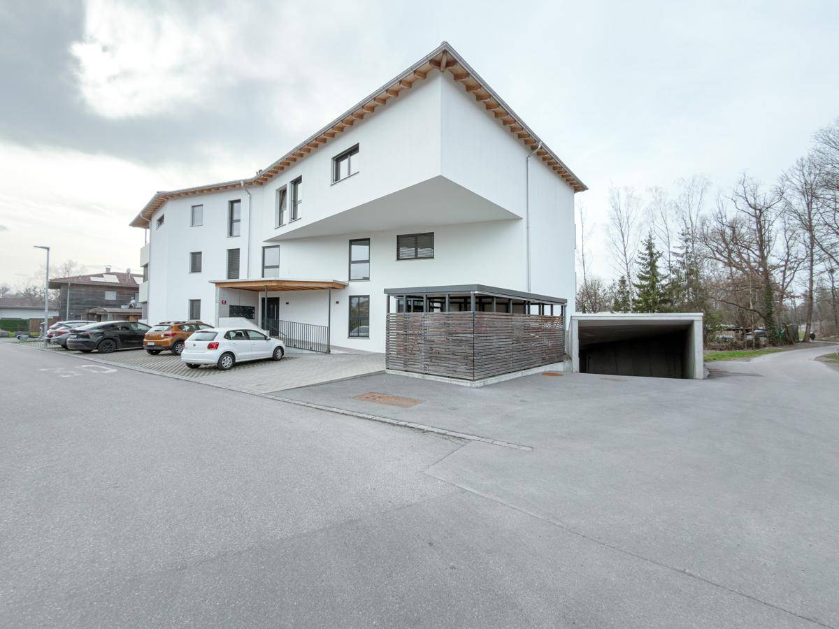 Modernes Mehrfamilienhaus mit weißer Fassade, Parkplätzen und überdachtem Carportbereich.