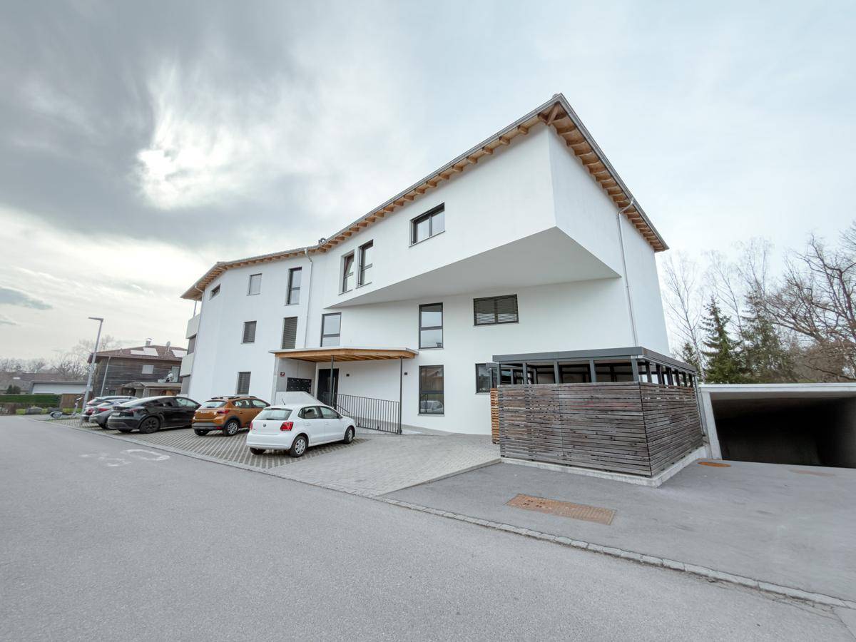 Ansicht des modernen Wohngebäudes mit weißer Fassade, Eingangsbereich und Parkmöglichkeiten.