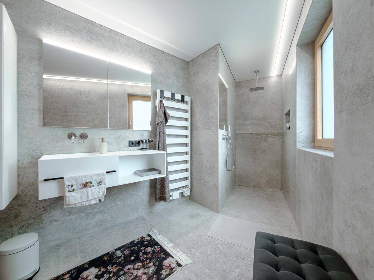 Modernes Badezimmer mit grauen Fliesen, schwebendem Waschtisch, begehbarer Dusche und Fenster.