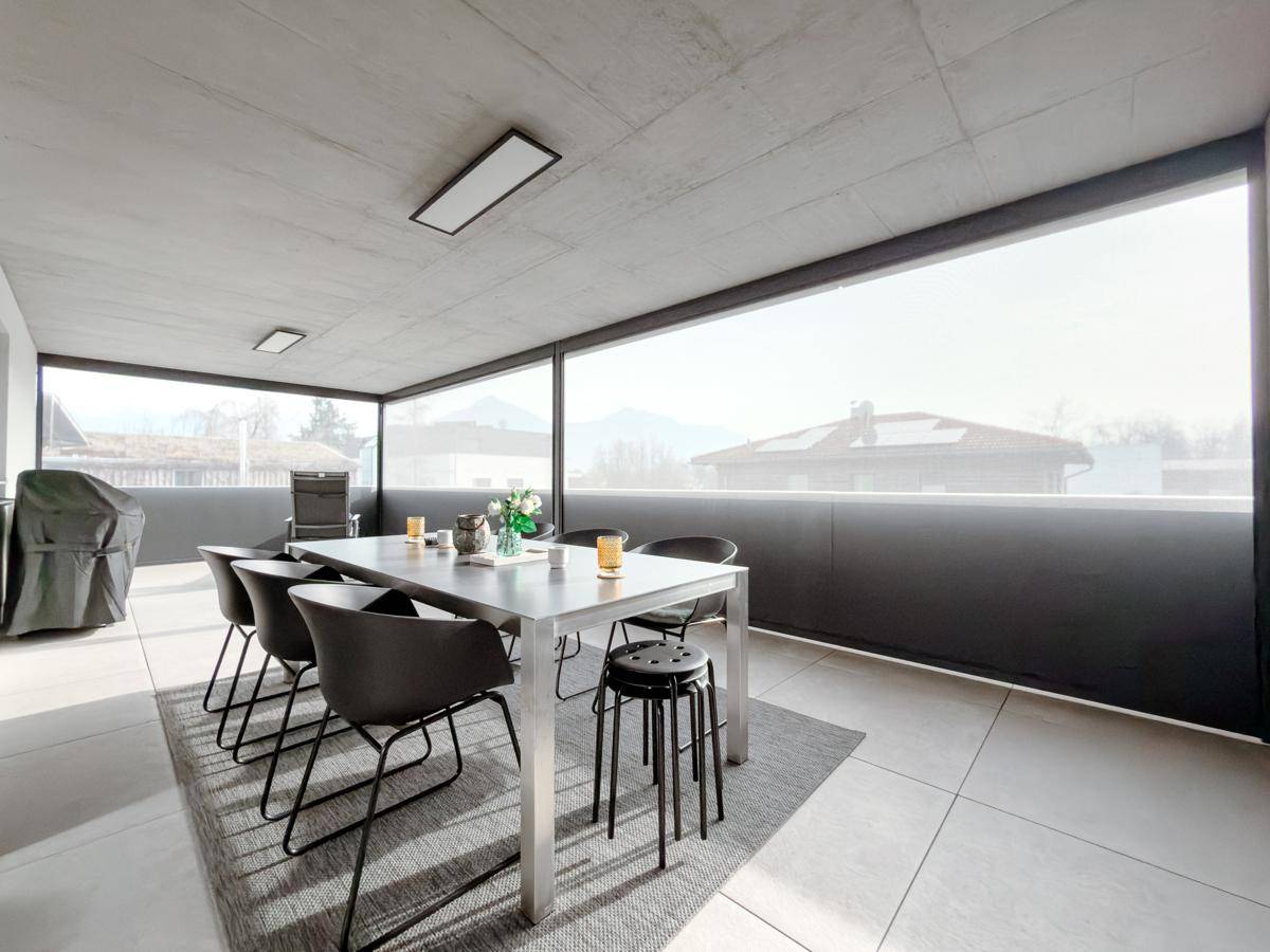 Geräumige überdachte Terrasse mit Esstisch, modernen Möbeln und weitem Blick auf die Berge.