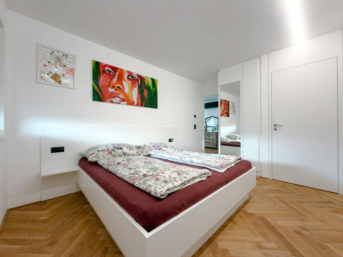 Modernes Schlafzimmer mit Doppelbett, Fischgrätparkett, farbenfrohem Kunstwerk und Spiegelschrank.