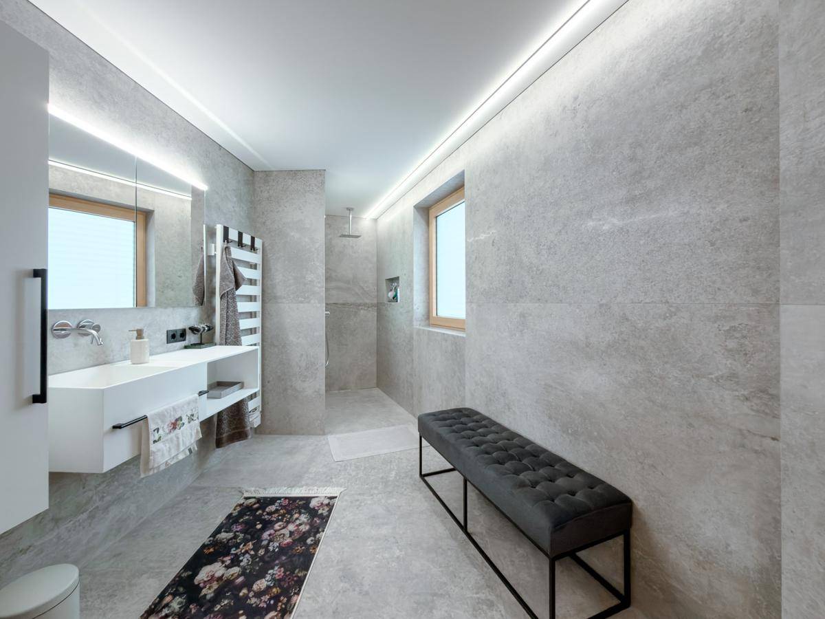 Modernes Badezimmer mit großen grauen Fliesen, begehbarer Dusche, Einzelwaschbecken und Fenster.