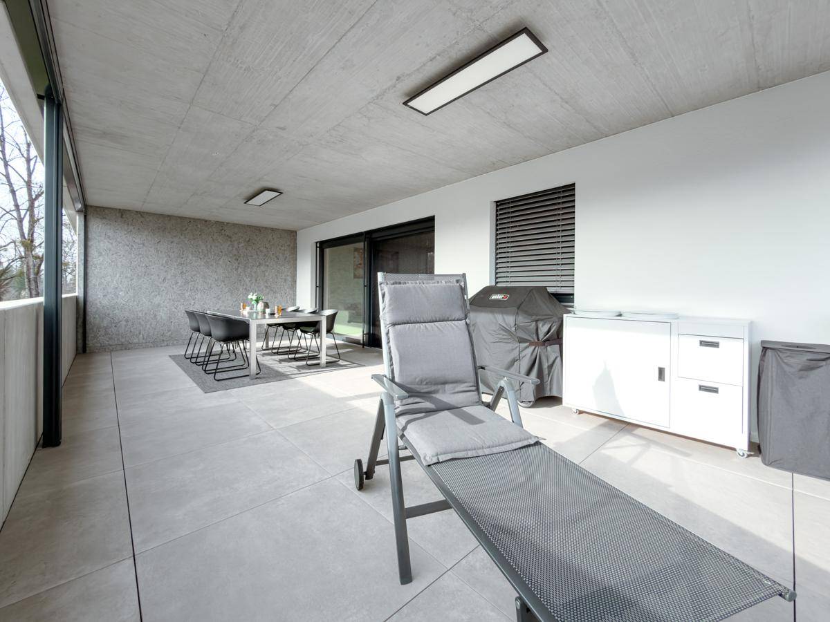 Geräumige überdachte Terrasse mit Liegestuhl, Essbereich, Grill und praktischen Außenmöbeln.