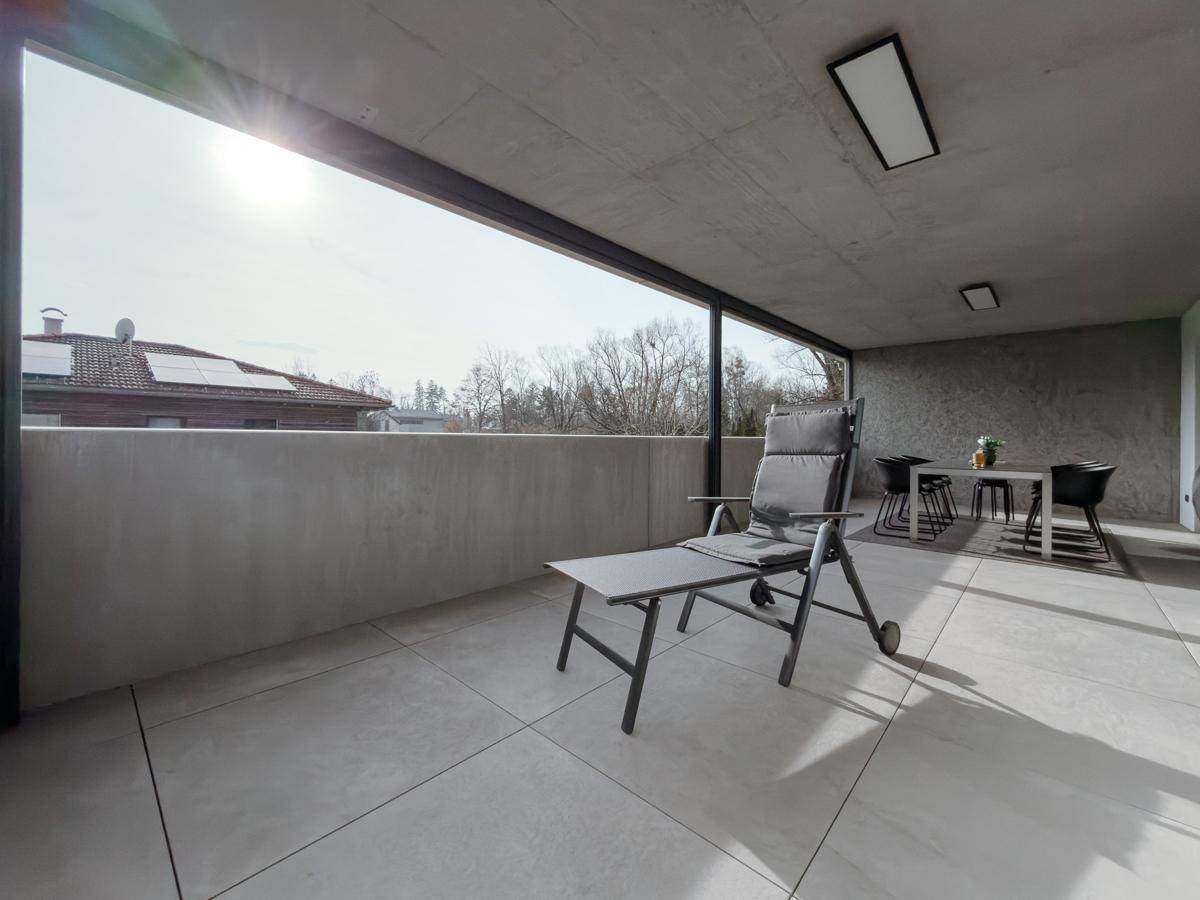Überdachte Terrasse mit Liegestuhl, Essbereich und sonnigem Ausblick auf die Umgebung.