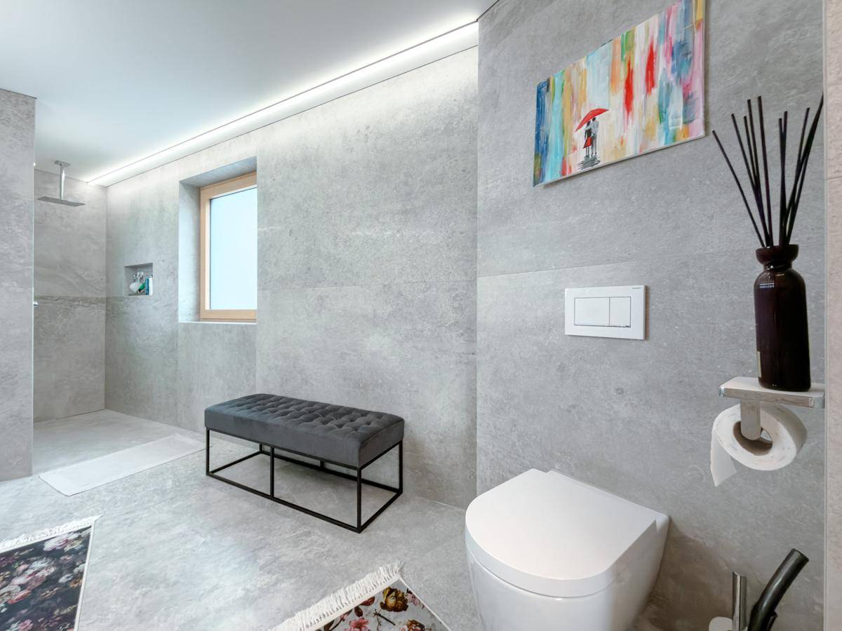 Modernes Badezimmer mit grauen Fliesen, wandhängendem WC und geräumiger begehbarer Dusche.