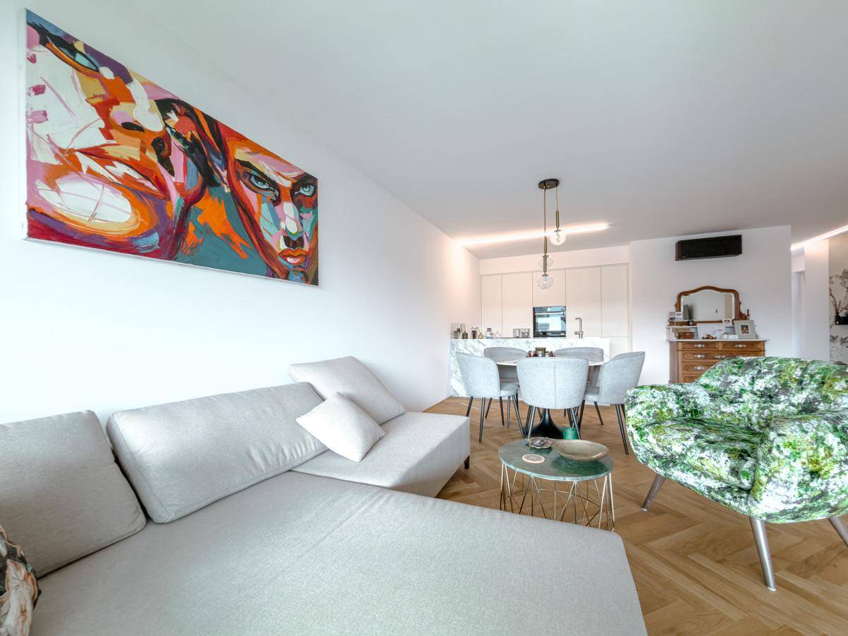 Heller Wohnbereich mit moderner Couch, farbenfrohem Bild und offenem Konzept zur Küche.