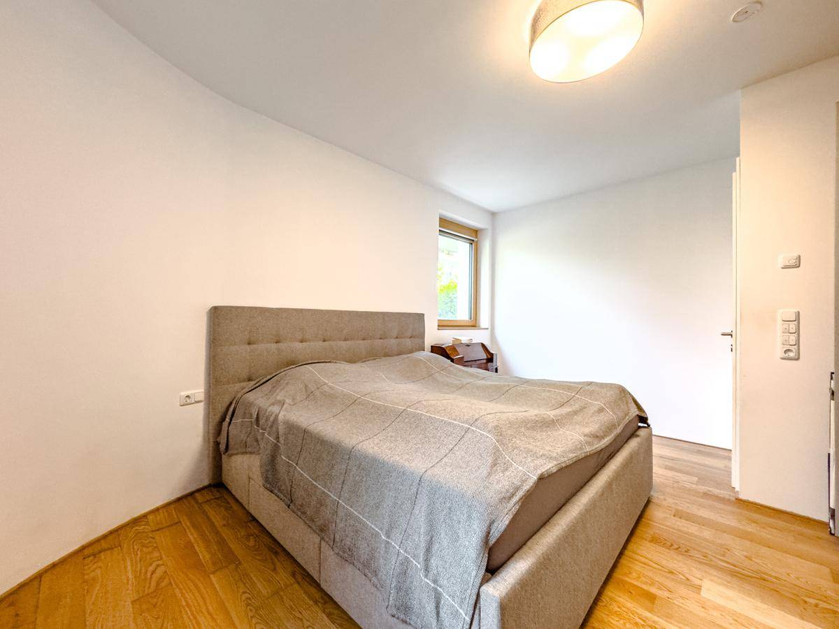 Helles Schlafzimmer mit Doppelbett, Holzfußboden und schlichter Einrichtung, mit viel Tageslicht.