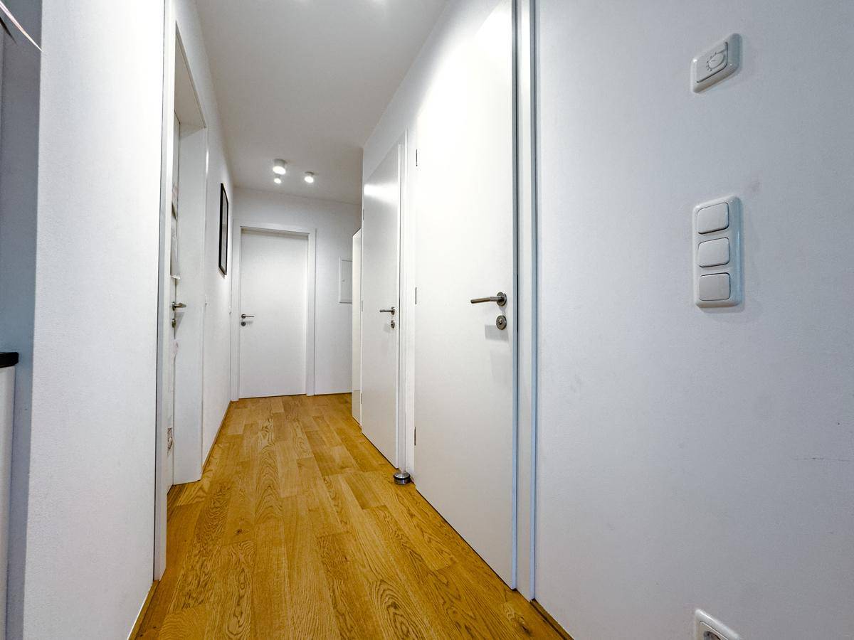 Langer, heller Flur mit Holzfußboden und mehreren weißen Türen, die zu den Zimmern führen.