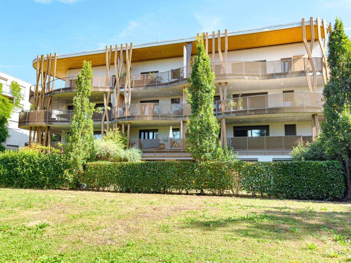 Elegantes Mehrfamilienhaus mit markanten Holzelementen und gepflegter Grünfläche im Vordergrund.