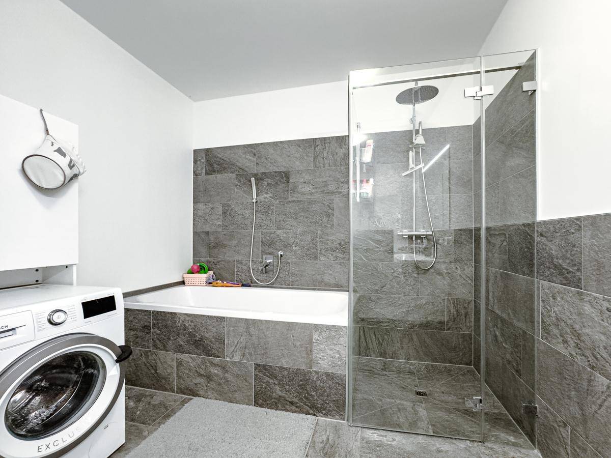 Modernes Badezimmer mit Badewanne, begehbarer Dusche und Waschmaschine, praktisch eingerichtet.
