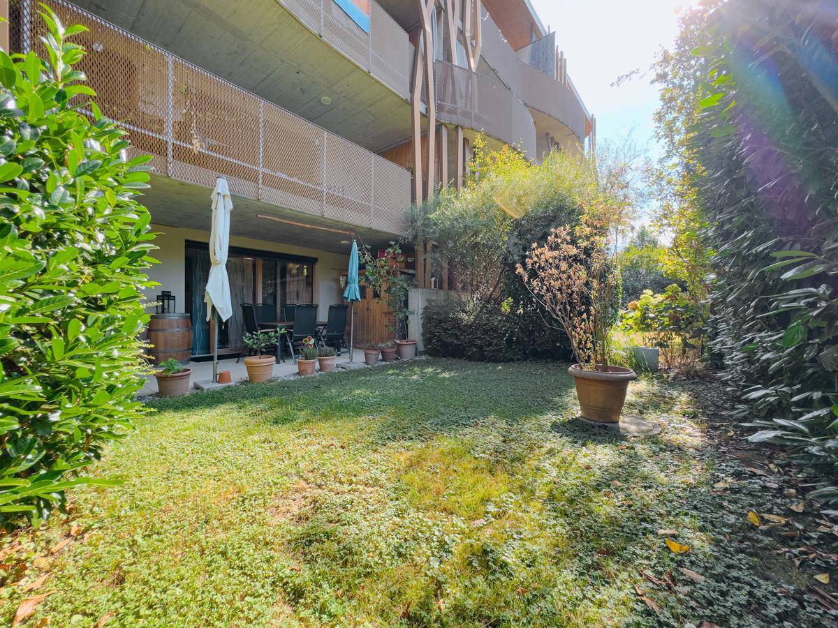 Gepflegter Gartenbereich mit Rasenfläche und angrenzender Terrasse unter einem Balkon.