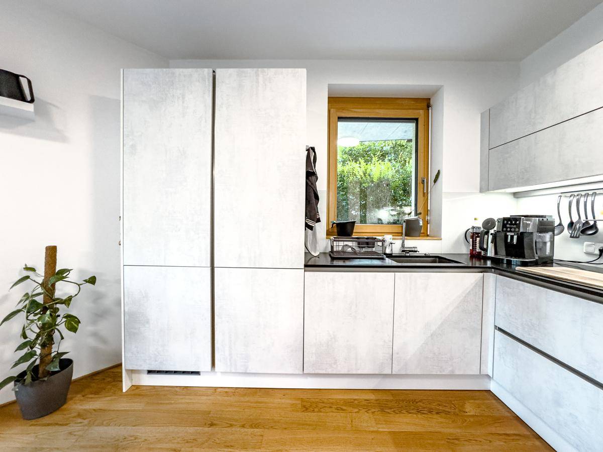 Moderne Küche mit hellen Fronten, Holzboden und Fenster mit Blick ins Grüne.