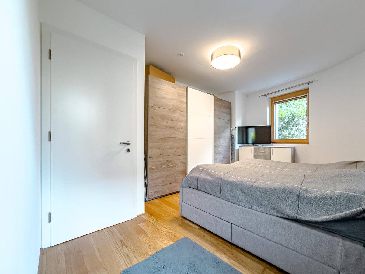 Helles Schlafzimmer mit Doppelbett, Holzfußboden und großem Schiebetürenschrank, gut beleuchtet.