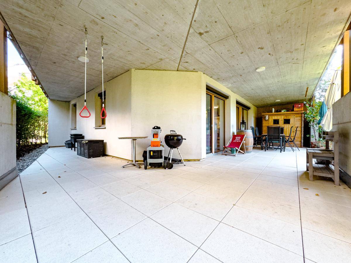 Große überdachte Terrasse mit Fliesenboden, Grill und Sitzgelegenheiten im Freien.