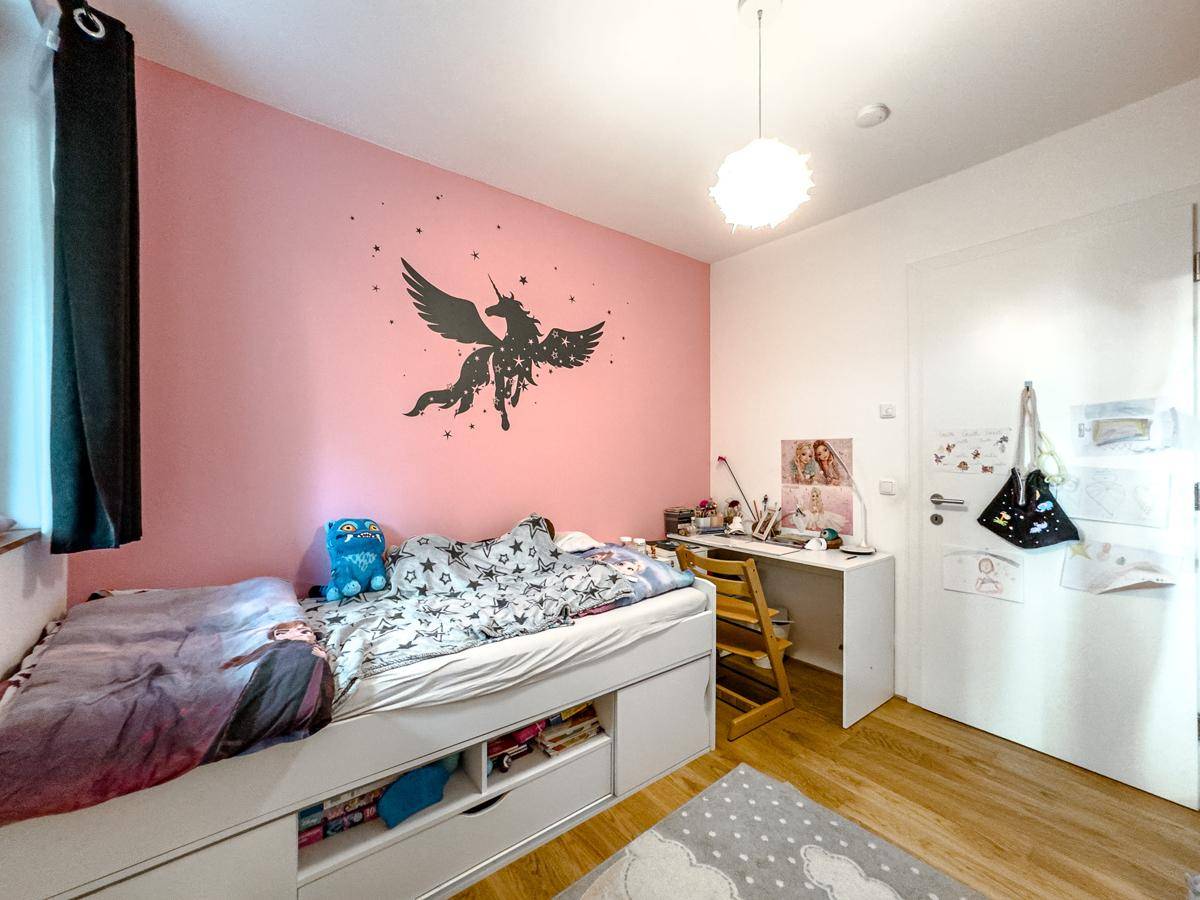 Kinderzimmer mit rosa Wand, Einzelbett und Schreibtisch, hell und freundlich gestaltet.