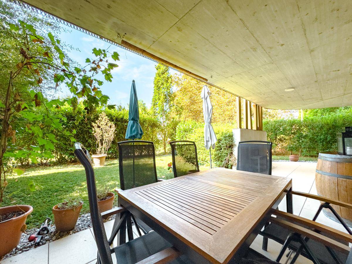 Gemütliche überdachte Terrasse mit Holztisch und Gartenblick, ideal zum Entspannen im Freien.