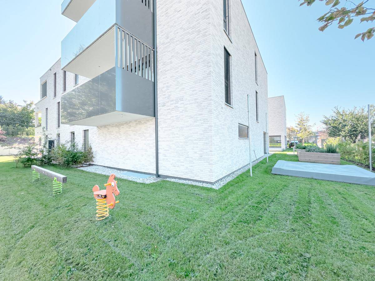 Grüner Außenbereich mit Spielgeräten und Rasenfläche, ideal für Familien mit Kindern.