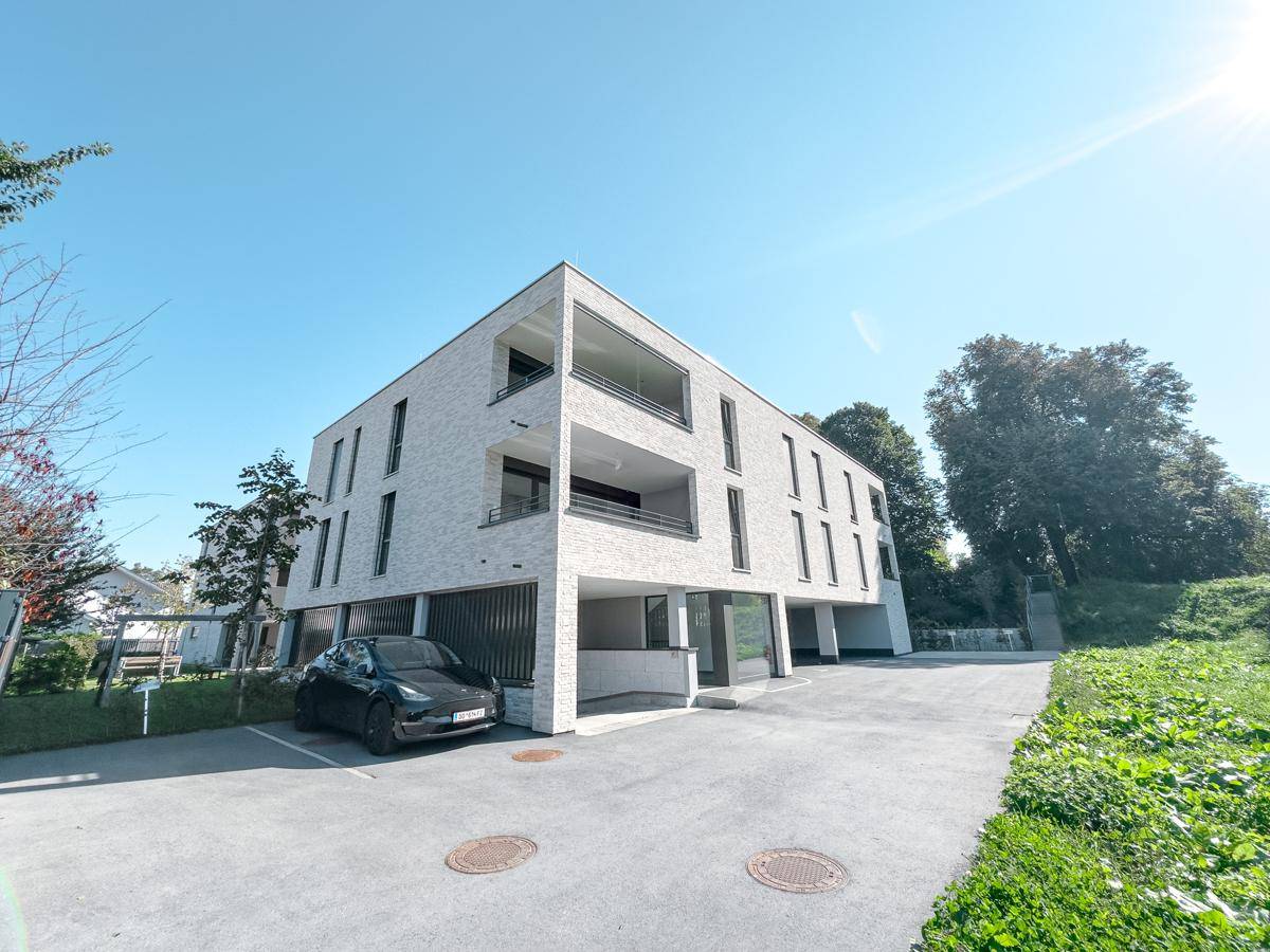 Modernes Wohngebäude mit Tiefgaragenzufahrt und Außenstellplätzen, umgeben von Grünflächen.