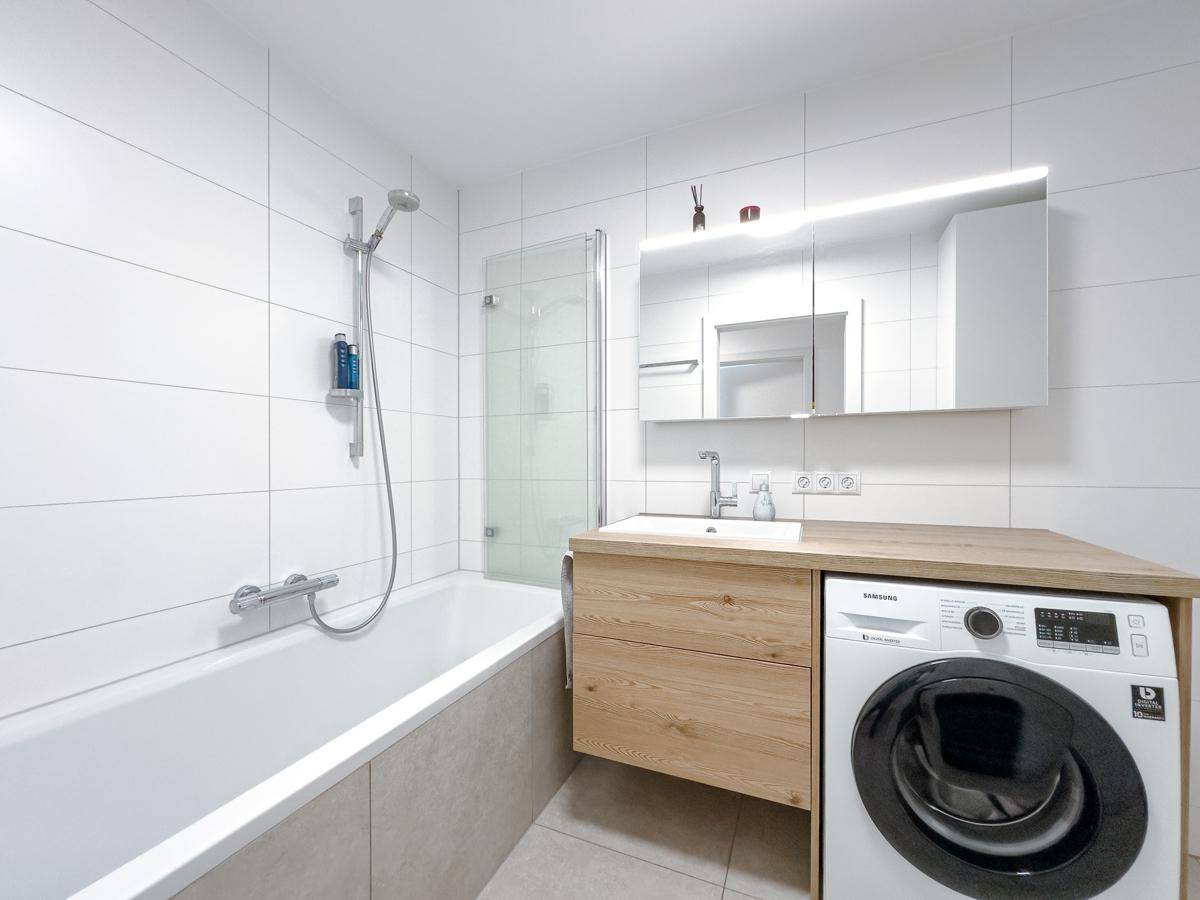 Modernes Badezimmer mit Badewanne, Dusche und integrierter Waschmaschine unter dem Waschtisch.