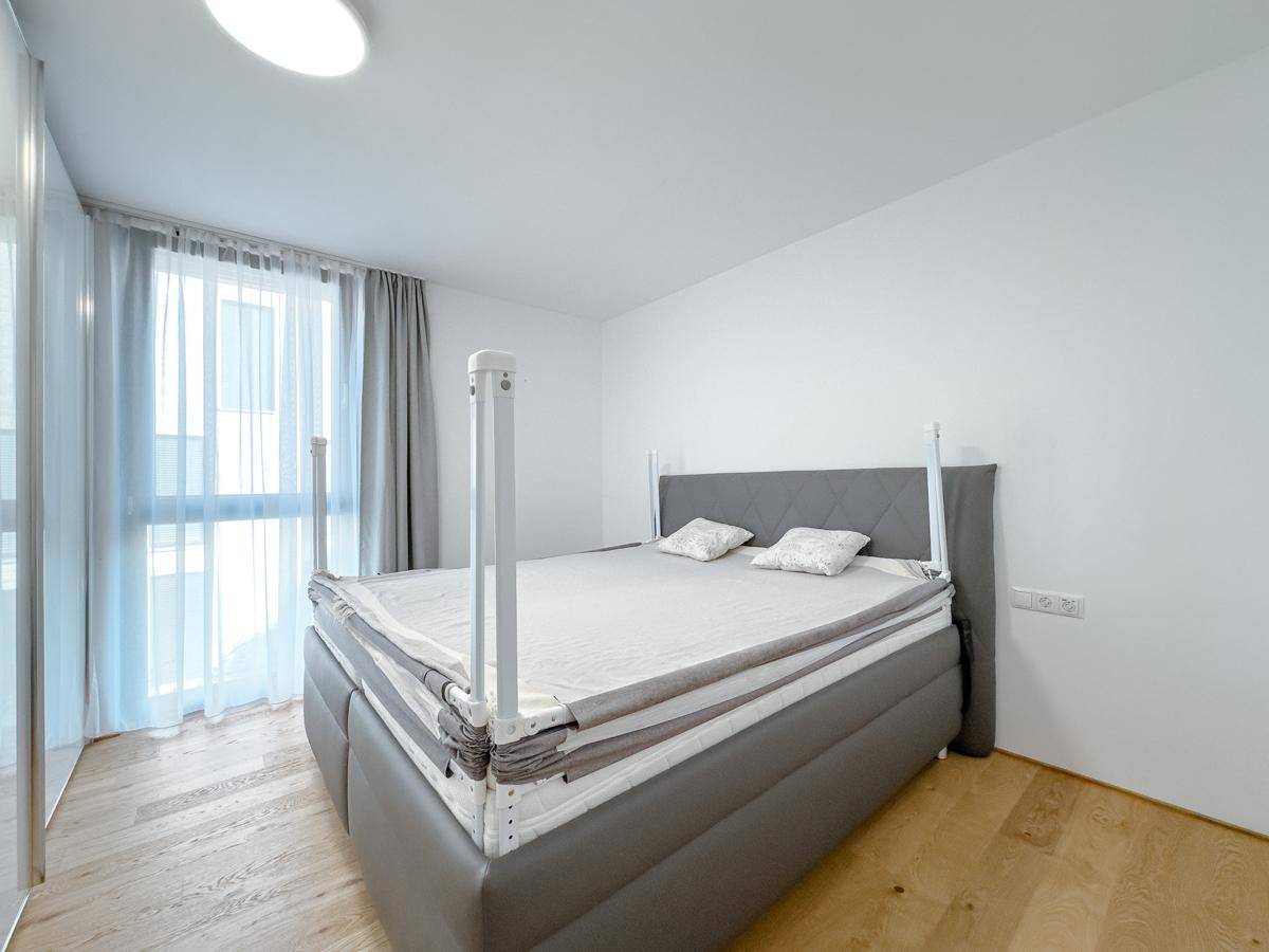 Geräumiges Schlafzimmer mit Doppelbett und Holzboden, durch große Fenster lichtdurchflutet.