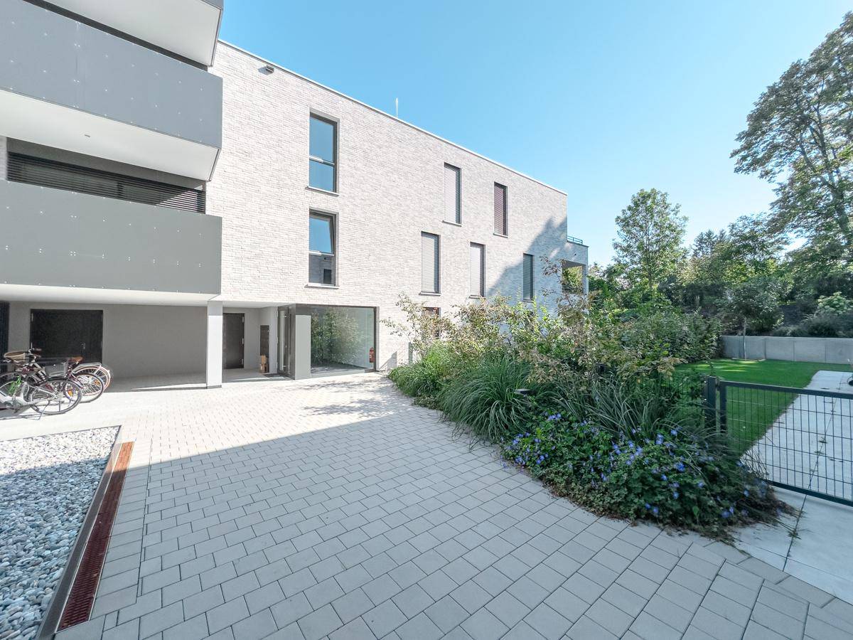 Außenbereich eines modernen Wohngebäudes mit gepflastertem Weg und bepflanzten Beeten.