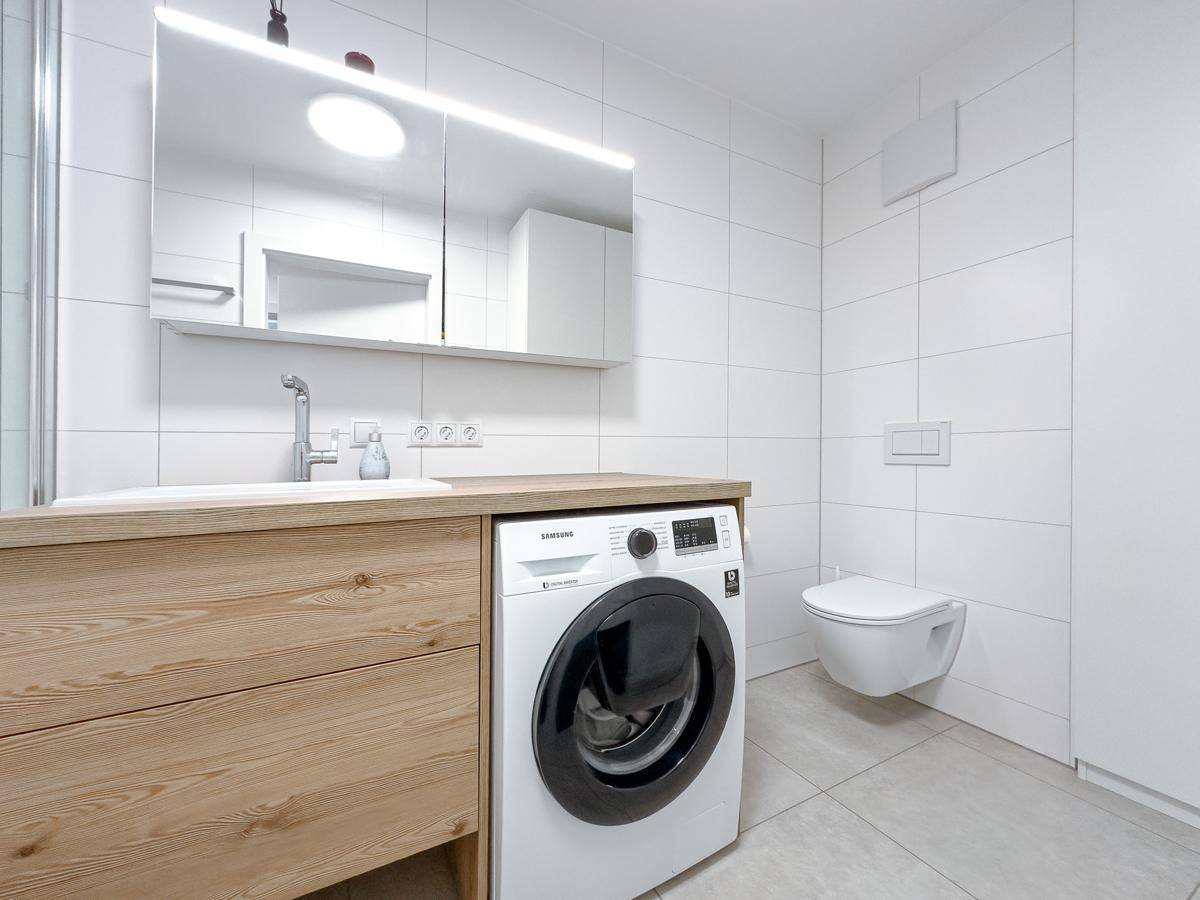 Helles Badezimmer mit modernem Waschtisch, integrierter Waschmaschine und wandhängendem WC.