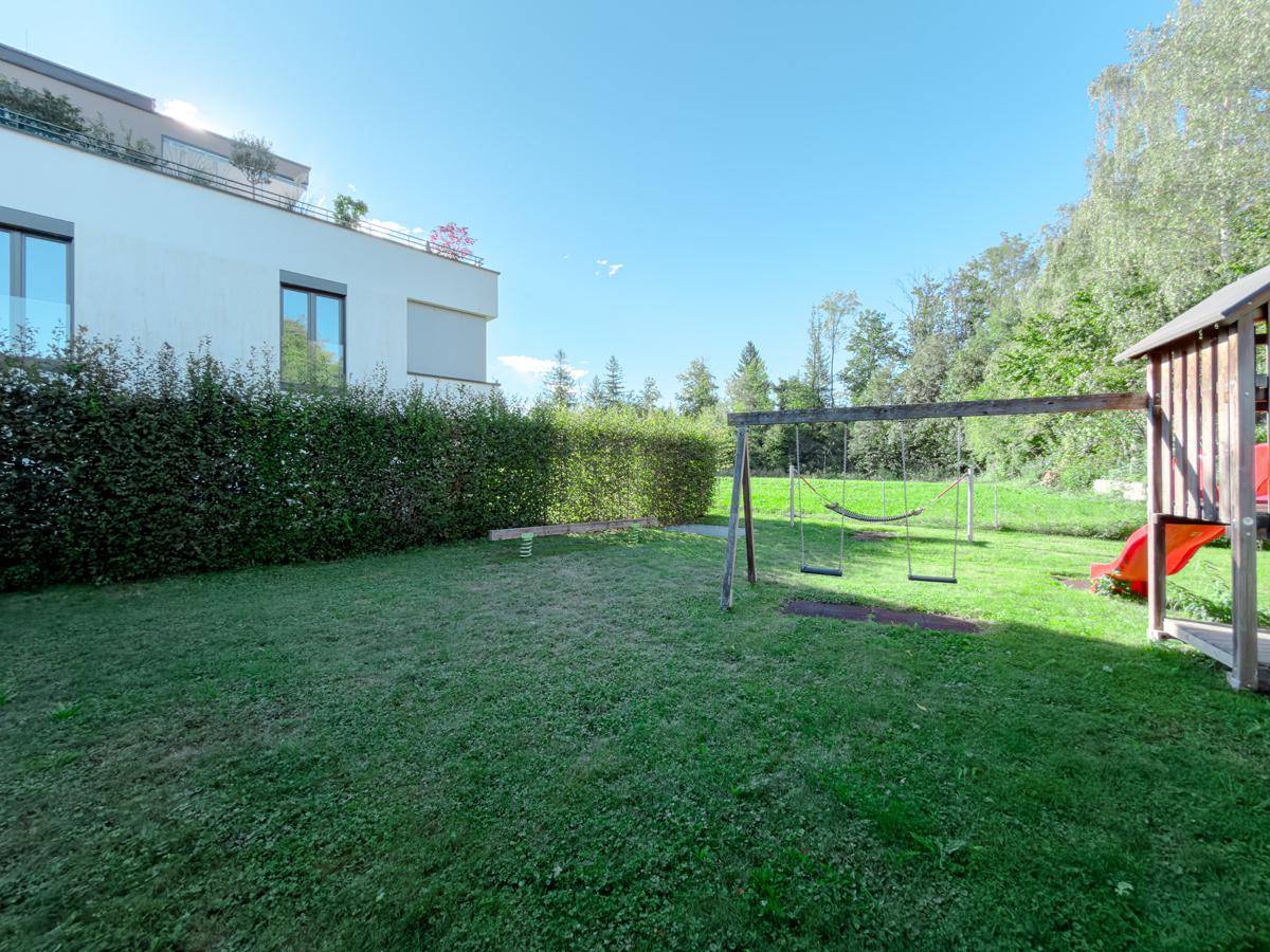 Grüner Garten mit Schaukeln und Rutsche, umgeben von einer Hecke.