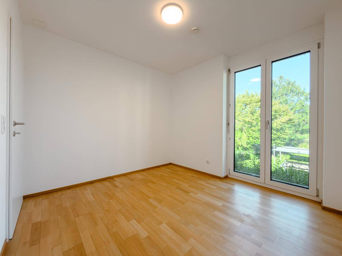 Lichtdurchflutetes Zimmer mit Parkettboden und Fensterfront zur Natur.