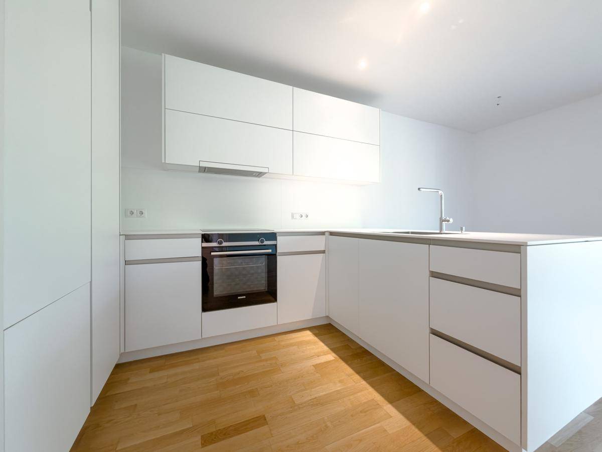 Weiße, grifflose Küche mit Backofen und Kochfeld, ideal für offene Wohnkonzepte.