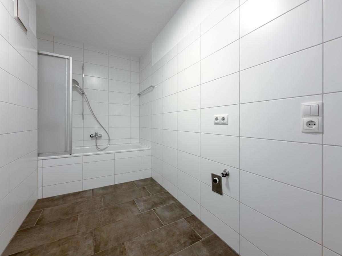 Modernes Badezimmer mit weißen Fliesen, Badewanne und Duschfunktion.