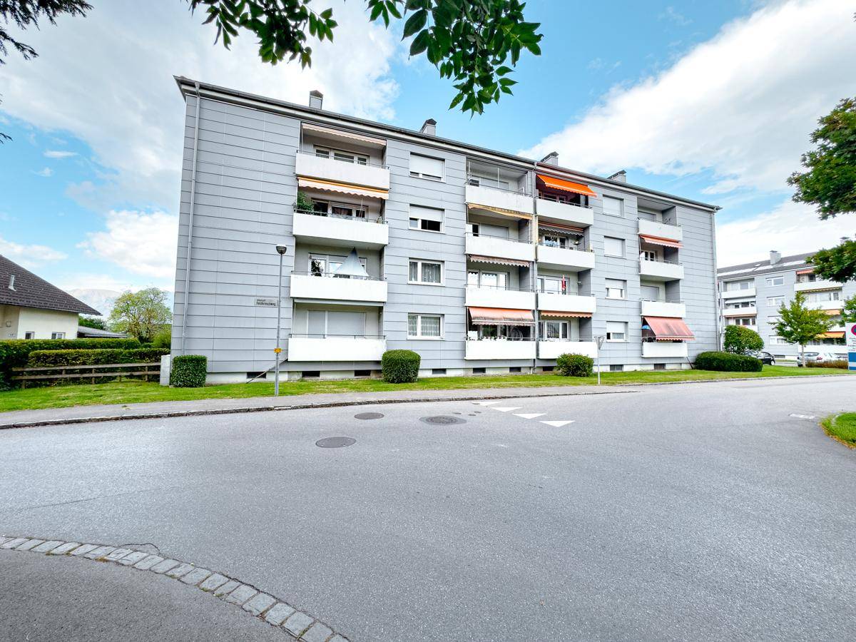 Ansicht des Mehrfamilienhauses von der Straße mit mehreren Balkonen und Markisen.