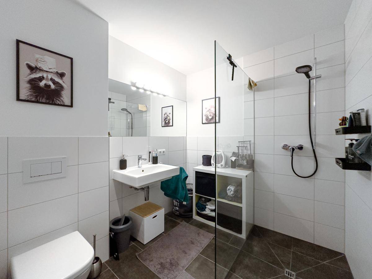 Modernes Badezimmer mit weiß gefliesten Wänden, ebenerdiger Dusche und Waschbecken.