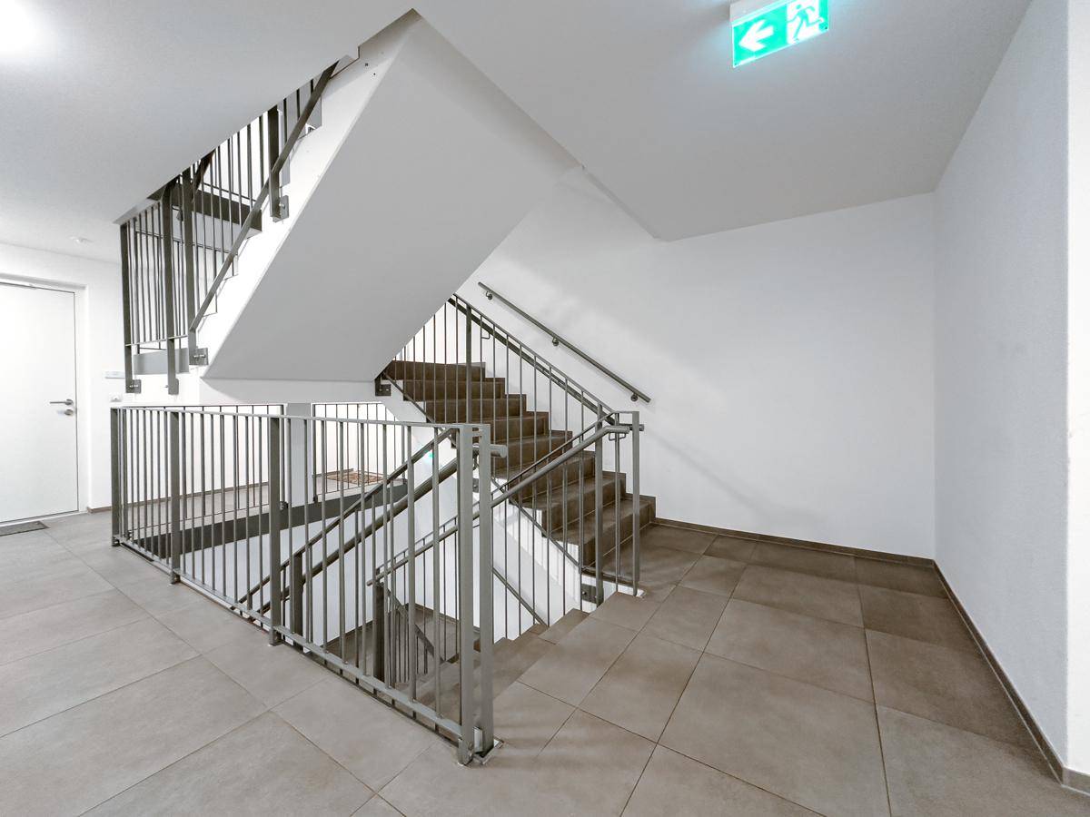 Heller Treppenaufgang in einem Mehrfamilienhaus mit Metallgeländer und Fliesenboden.
