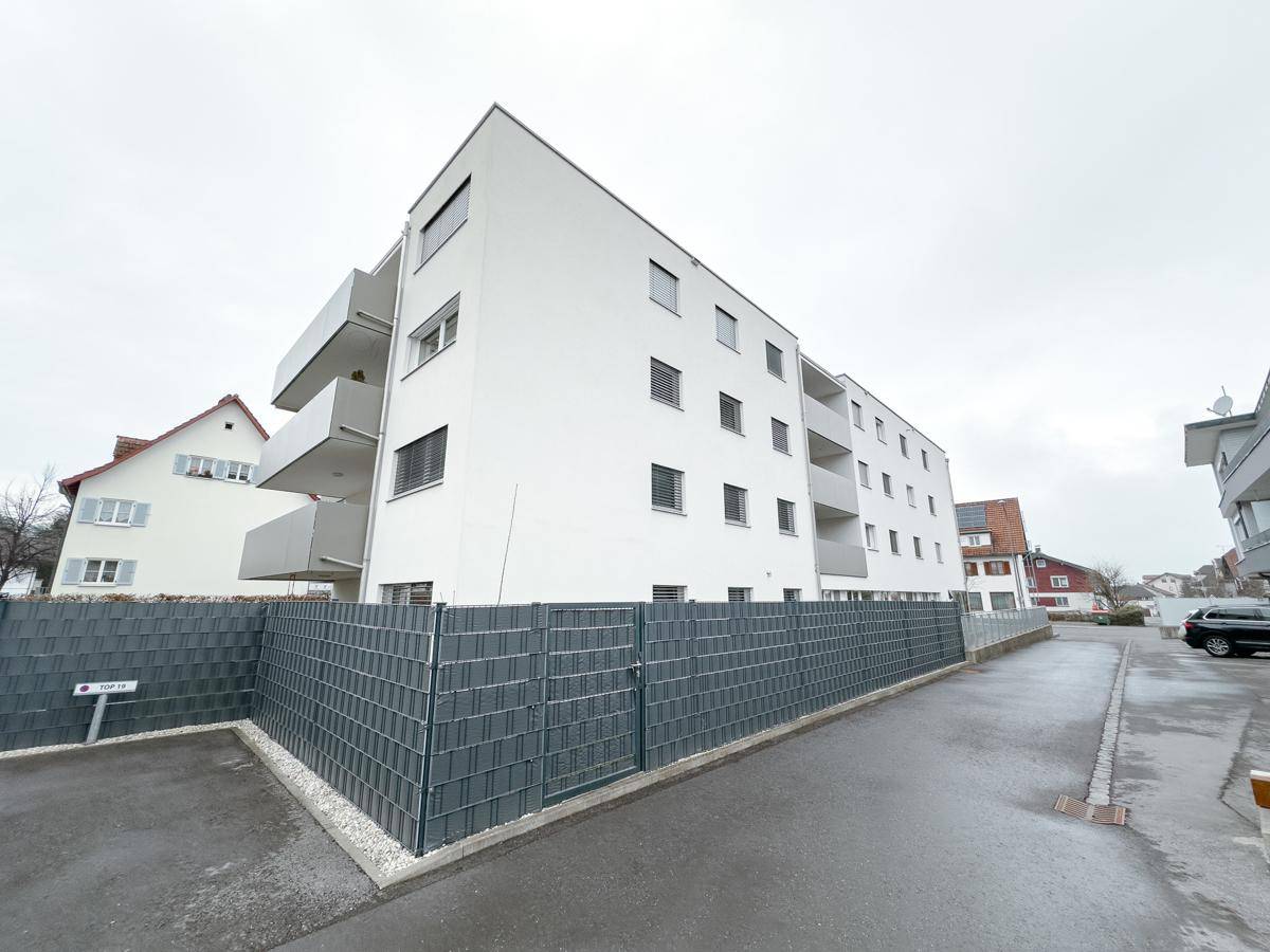 Seitenansicht eines modernen Gebäudes mit Balkonen und einem Zaun im Vordergrund.