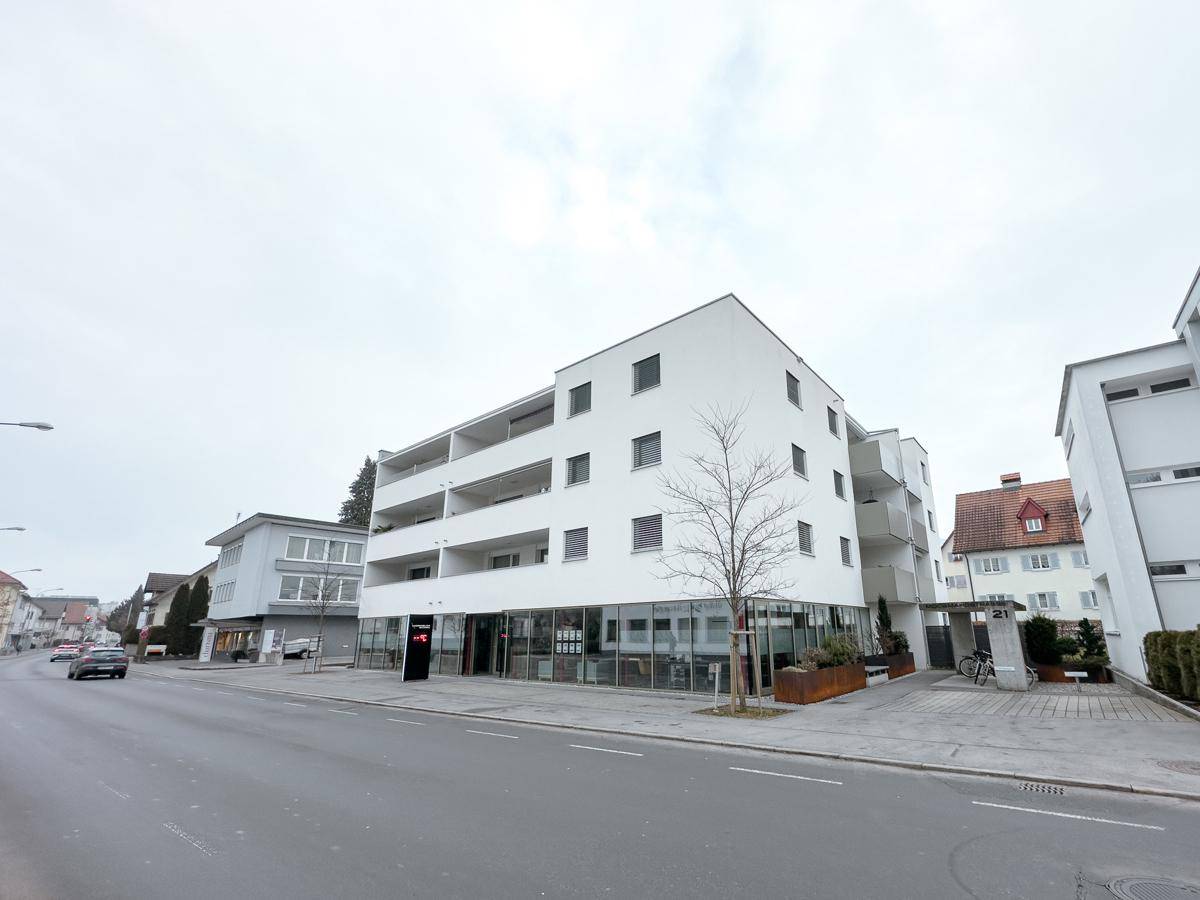 Modernes Wohn- und Geschäftshaus mit weißer Fassade und großen Fenstern an der Straße.