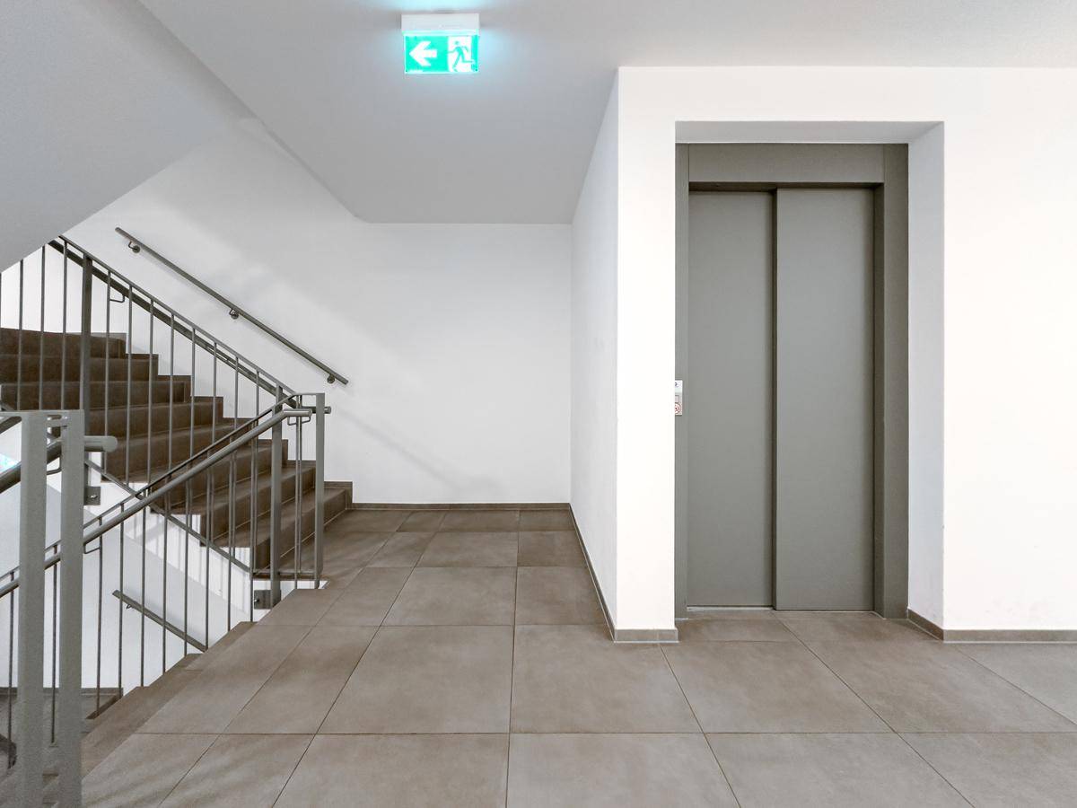 Treppenhaus mit Aufzug und Fliesenboden in einem modernen Wohngebäude.