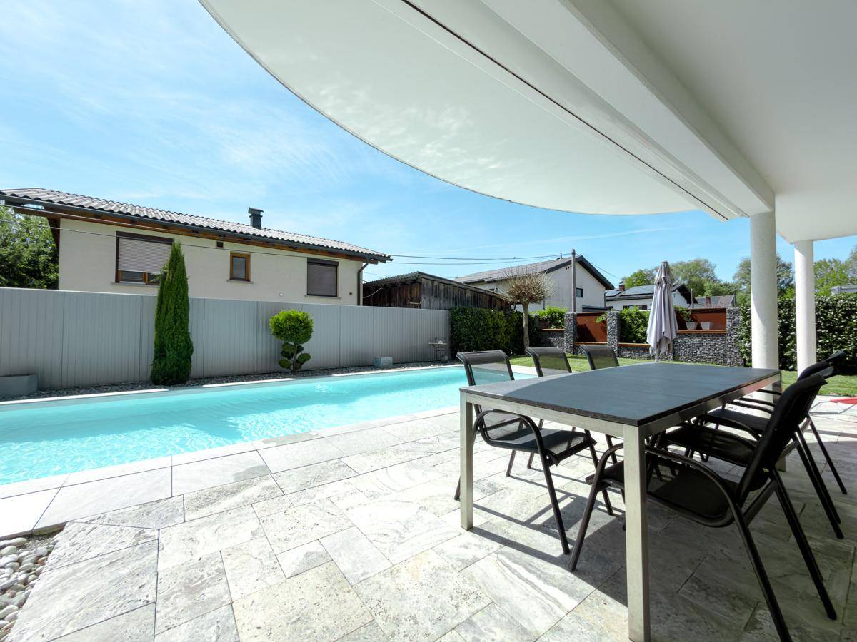 Sonnige Terrasse mit Essbereich und Pool, umgeben von einem gepflegten Garten.