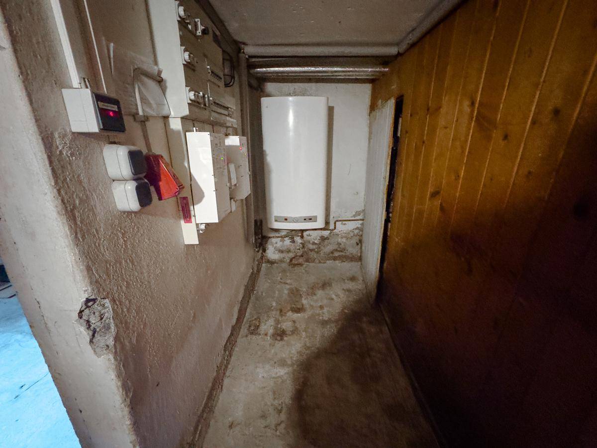 Schmaler Kellerflur mit Elektroinstallationen, Warmwasserbereiter und Holzverkleidung an der Wand.