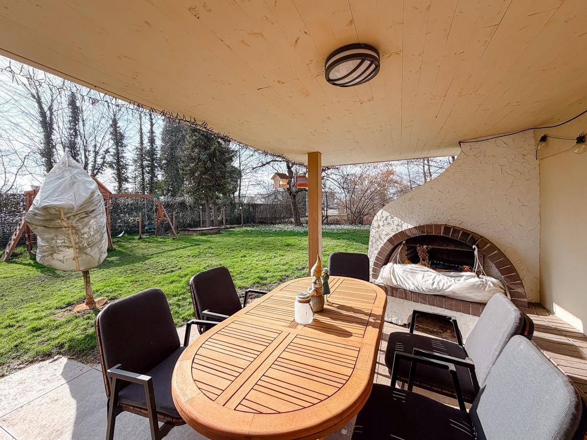 Gemütliche überdachte Terrasse mit Esstisch und integriertem Grill, umgeben von Grün.
