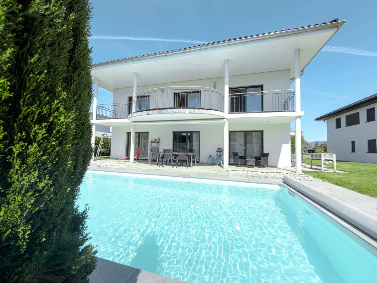 Außenbereich mit großem Pool, Rasenfläche und moderner Hausfassade.