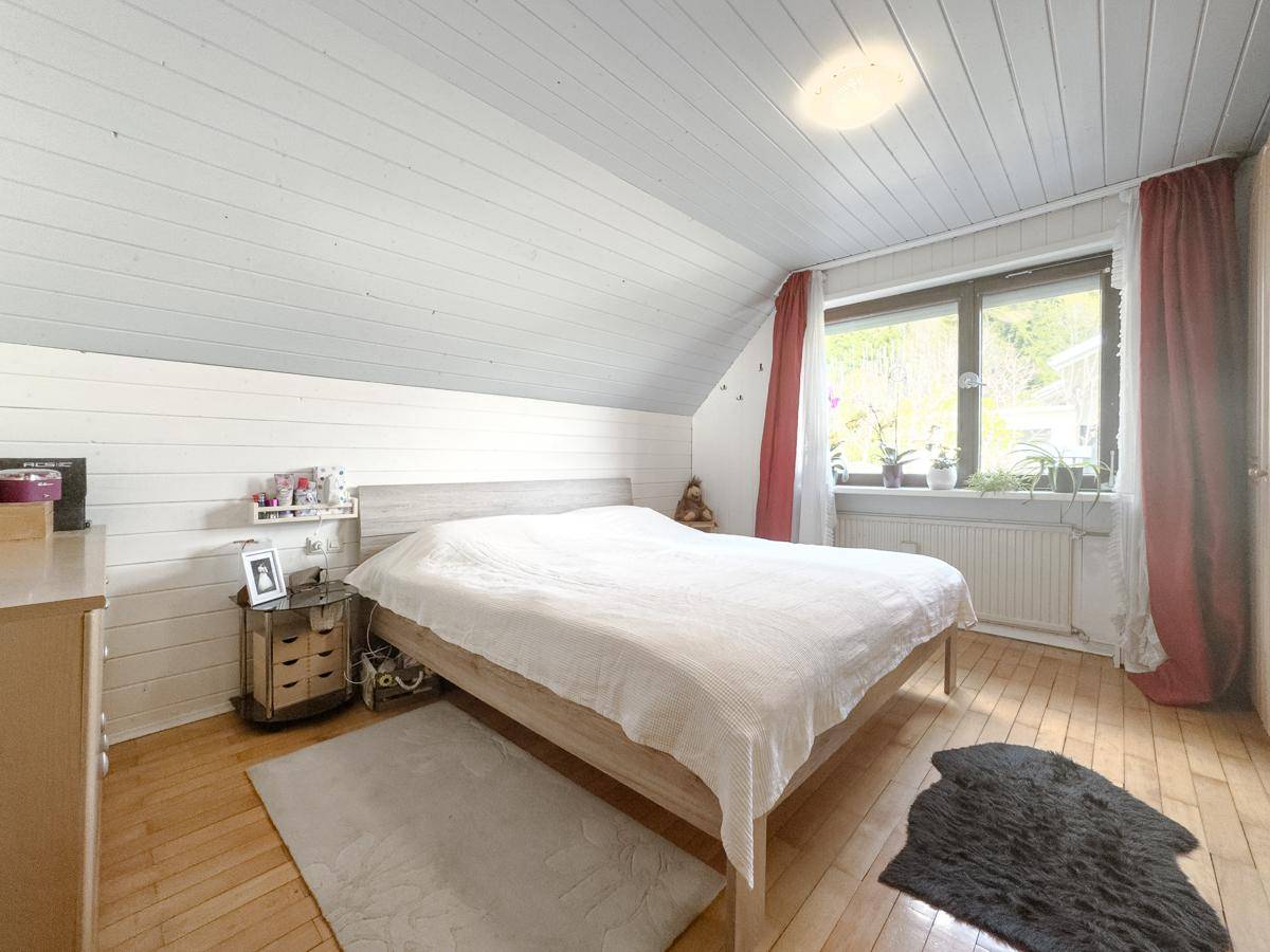 Helles Schlafzimmer im Dachgeschoss mit Holzwänden, Holzboden und Fenster mit Blick ins Grüne.
