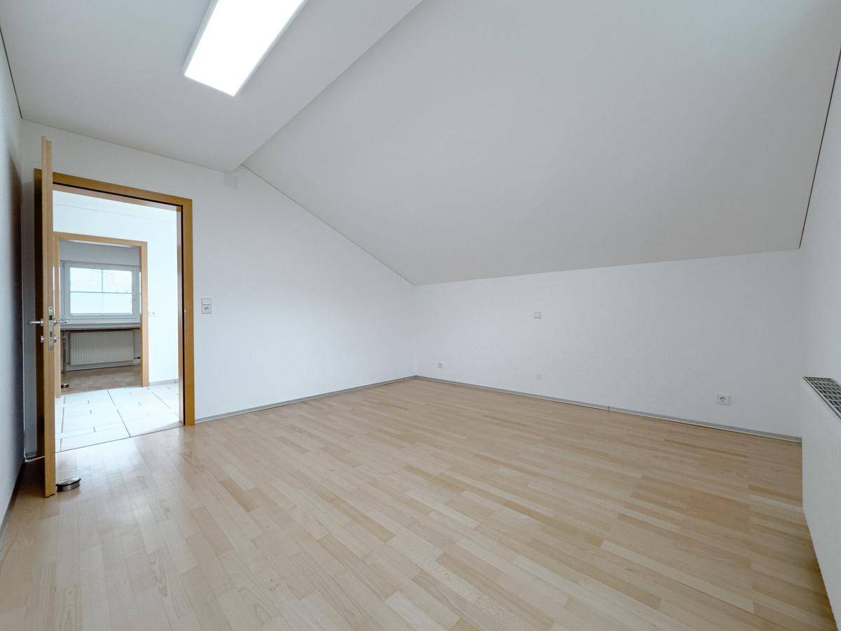 Helles Zimmer im Dachgeschoss mit Holzparkettboden, weiß gestrichenen Wänden und Dachschräge.