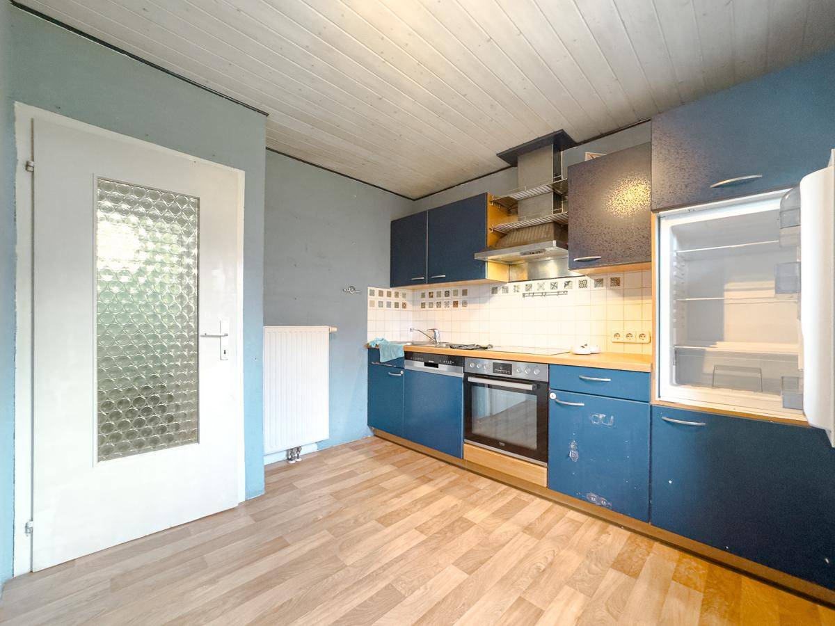 Funktionale Küche mit blauen Schränken, integrierten Geräten und Holzdeckenverkleidung.