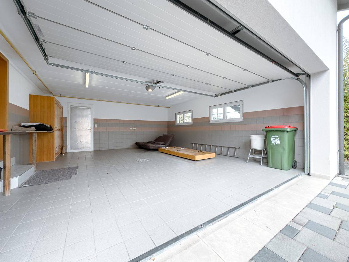 Geräumige Garage mit Fliesenboden, Fenstern und einem breiten Garagentor.