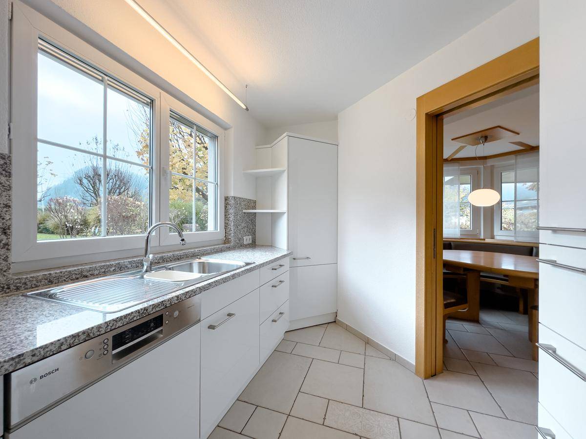 Moderne Küche mit weißen Schränken, Granitarbeitsplatte und Blick ins Grüne.