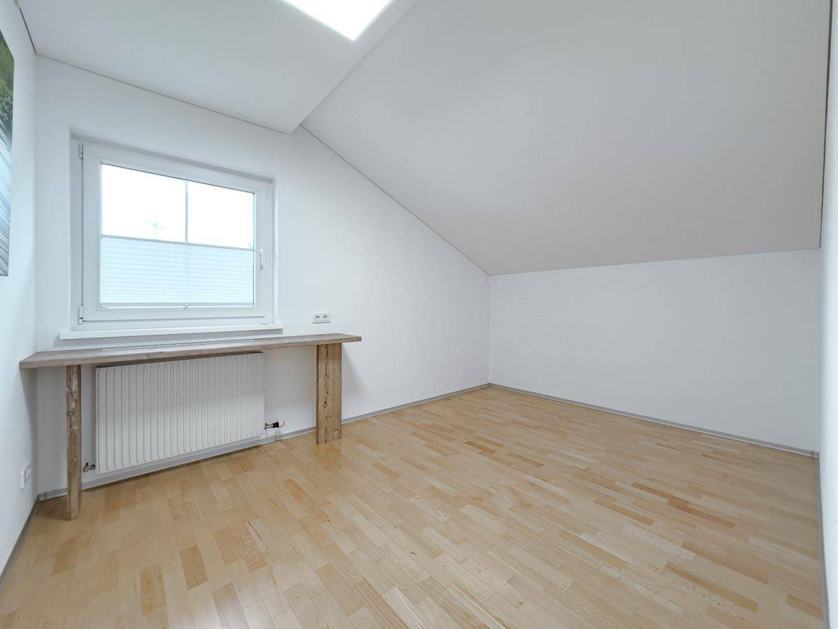 Helles Zimmer im Dachgeschoss mit Parkettboden, Heizkörper und Fenster mit Ausblick.