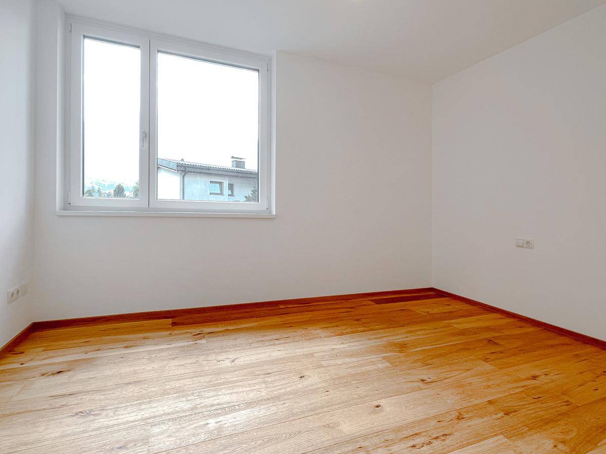Helles Schlafzimmer mit Holzparkettboden und einem großen Fenster, das viel Tageslicht hereinlässt.