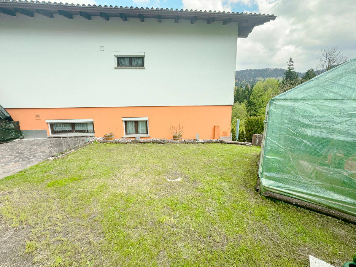 Gepflegter Rasenbereich neben dem Haus mit orangefarbener Fassade und Blick ins Grüne.