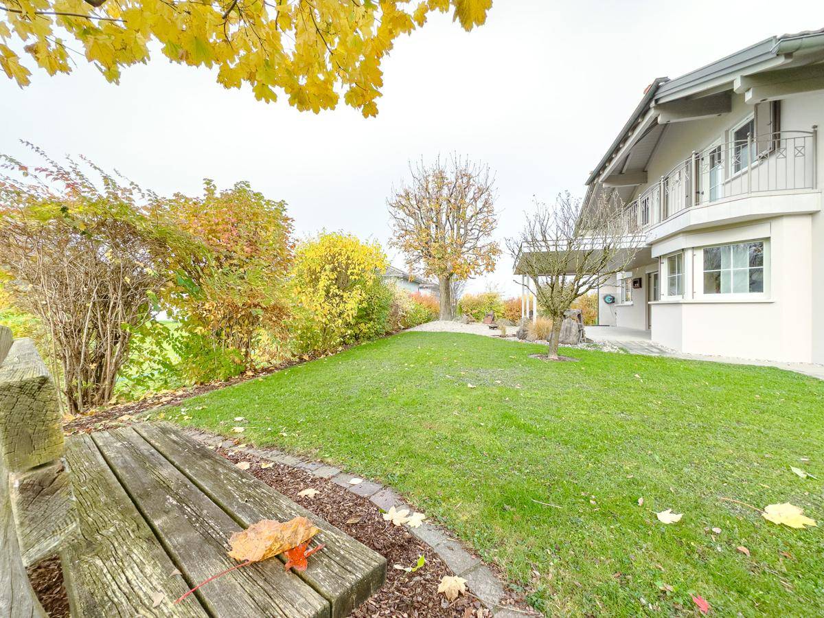 Gepflegter Garten mit Rasenfläche, Baumbestand und Sitzbank im Herbstlaub.